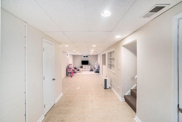 hall with a paneled ceiling, built in features, and light tile patterned flooring