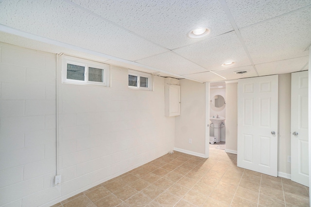 basement with a paneled ceiling, sink, and light tile patterned floors