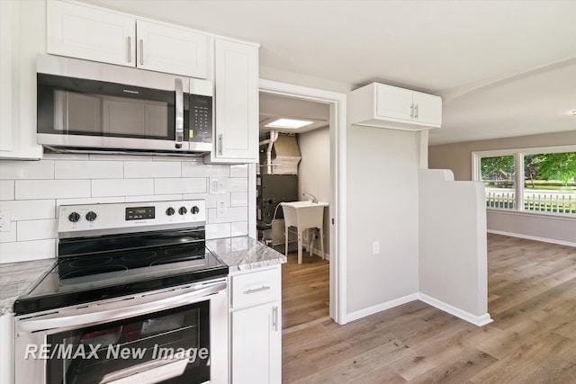 kitchen with light hardwood / wood-style flooring, decorative backsplash, appliances with stainless steel finishes, light stone counters, and white cabinetry