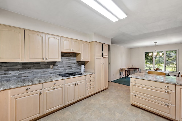 kitchen with light stone countertops, backsplash, decorative light fixtures, a notable chandelier, and black stovetop