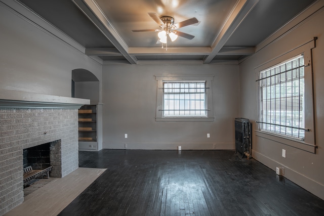 unfurnished living room with ceiling fan, dark wood-type flooring, coffered ceiling, a brick fireplace, and beamed ceiling