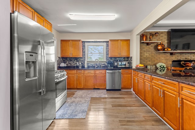 kitchen featuring appliances with stainless steel finishes, tasteful backsplash, sink, dark stone countertops, and light hardwood / wood-style floors