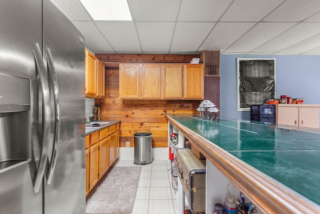 kitchen with wooden walls, a drop ceiling, and stainless steel refrigerator with ice dispenser