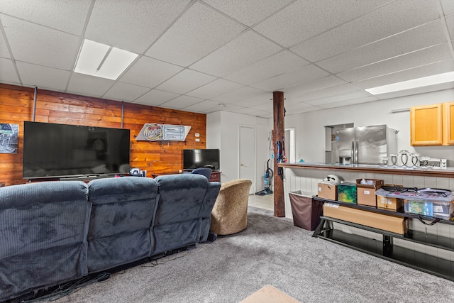 carpeted living room featuring a drop ceiling and wood walls