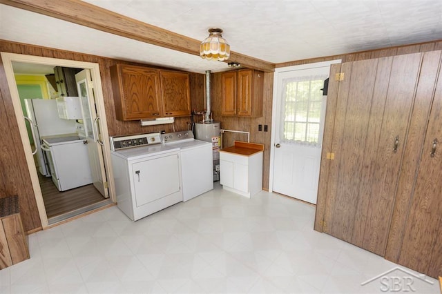 laundry room featuring cabinets, water heater, wood walls, and washing machine and clothes dryer