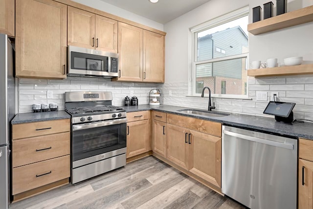 kitchen with appliances with stainless steel finishes, tasteful backsplash, sink, light brown cabinets, and light hardwood / wood-style flooring