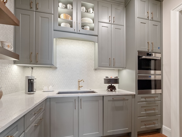 kitchen featuring light stone countertops, tasteful backsplash, gray cabinetry, and sink