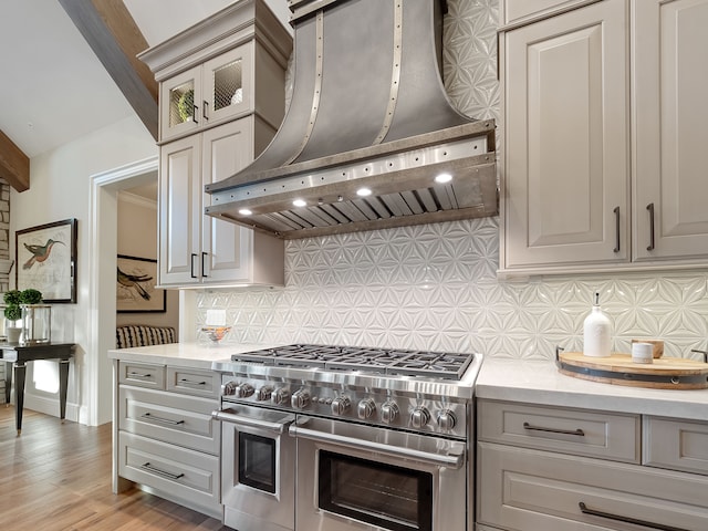 kitchen with gray cabinetry, range with two ovens, wall chimney range hood, decorative backsplash, and light hardwood / wood-style floors