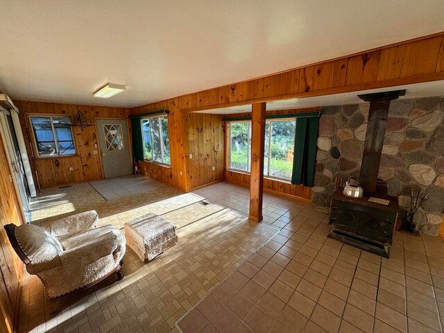unfurnished living room featuring light tile patterned floors, a wood stove, and wood walls