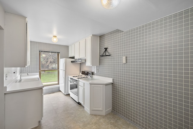 kitchen with white cabinets, white appliances, sink, and tile walls