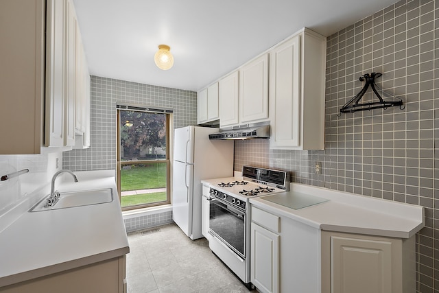 kitchen with sink, light tile patterned floors, white appliances, white cabinets, and tile walls