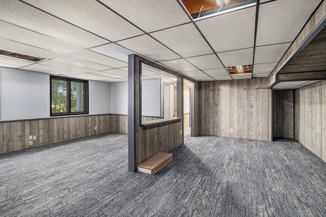 basement featuring a paneled ceiling and wood walls