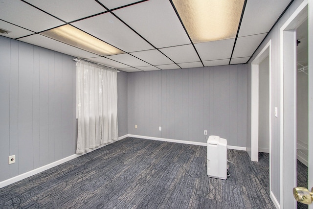 basement with a paneled ceiling, wooden walls, and dark wood-type flooring