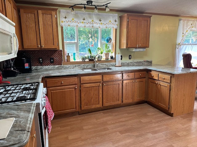 kitchen with crown molding, white appliances, kitchen peninsula, and sink