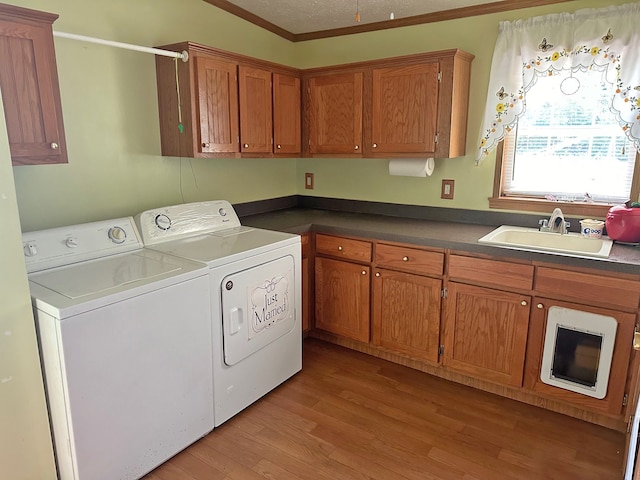 laundry area with sink, crown molding, cabinets, light hardwood / wood-style floors, and washing machine and dryer