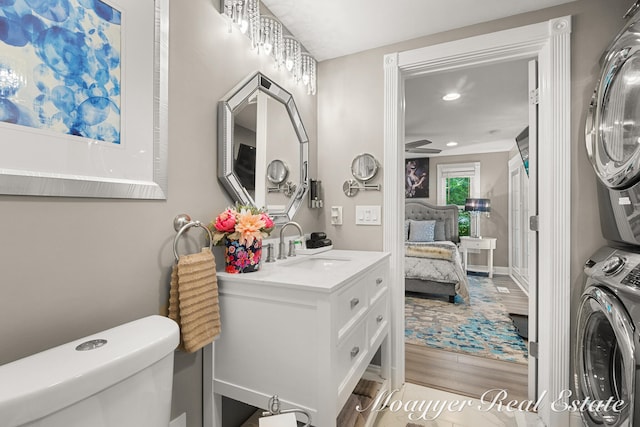 bathroom with vanity, stacked washer and clothes dryer, hardwood / wood-style flooring, ceiling fan, and toilet