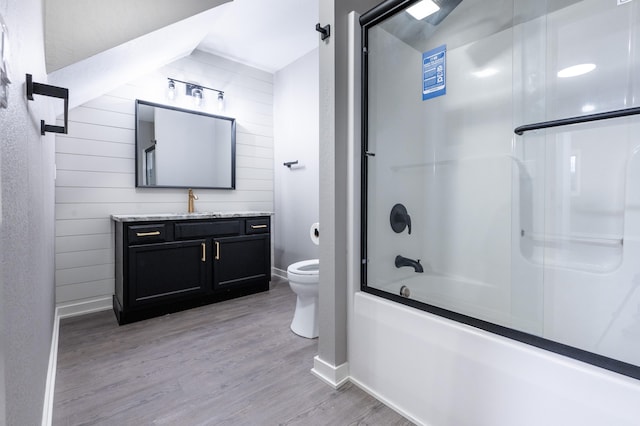 full bathroom featuring vanity, enclosed tub / shower combo, hardwood / wood-style floors, toilet, and wood walls