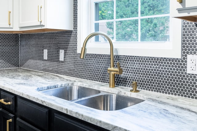 kitchen with backsplash, light stone counters, white cabinetry, and sink