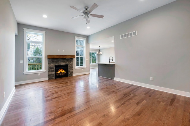 unfurnished living room with a fireplace, hardwood / wood-style floors, and ceiling fan with notable chandelier