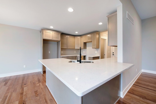 kitchen with kitchen peninsula, light brown cabinets, light hardwood / wood-style floors, and sink