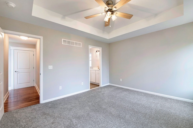 unfurnished bedroom featuring ceiling fan, dark carpet, and a tray ceiling