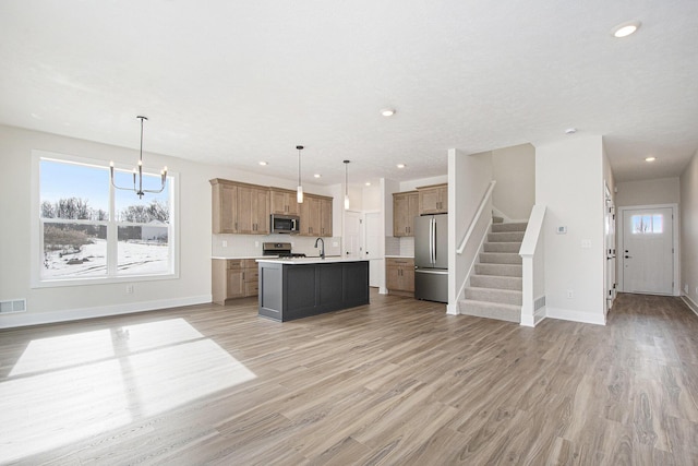 kitchen with stainless steel appliances, a healthy amount of sunlight, a center island with sink, and decorative light fixtures