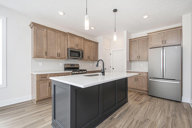 kitchen featuring sink, decorative light fixtures, a center island with sink, light hardwood / wood-style flooring, and stainless steel appliances