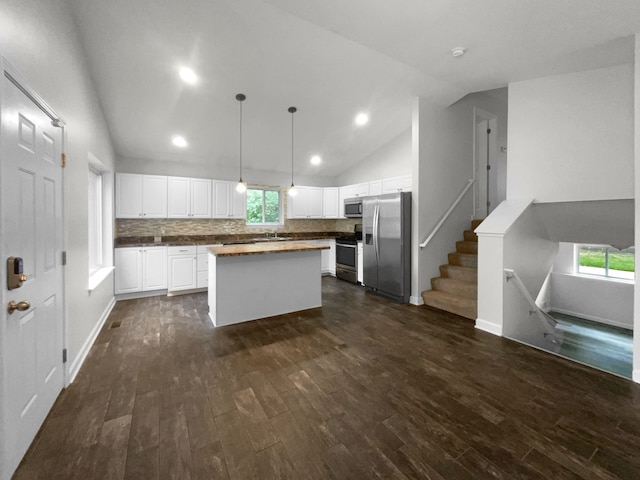 kitchen with dark wood-type flooring, stainless steel appliances, decorative light fixtures, lofted ceiling, and white cabinets