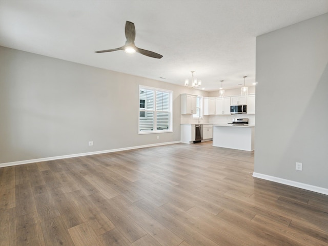 unfurnished living room with sink, ceiling fan with notable chandelier, and light wood-type flooring