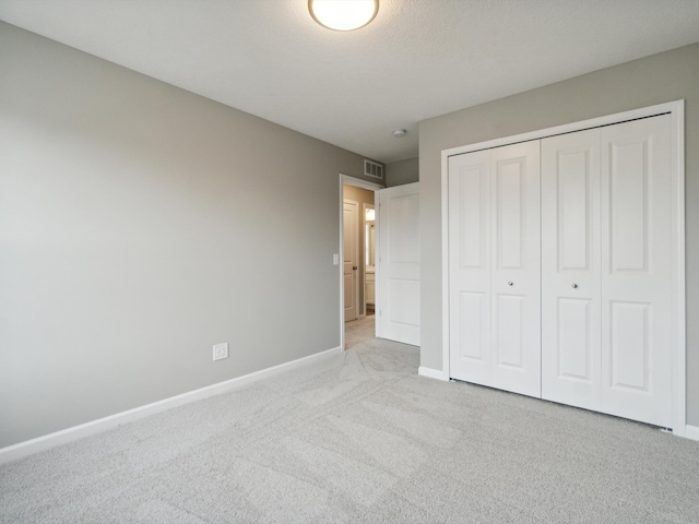 unfurnished bedroom featuring light carpet, a textured ceiling, and a closet