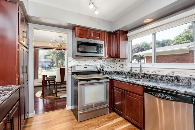 kitchen with sink, decorative backsplash, dark stone countertops, light wood-type flooring, and appliances with stainless steel finishes