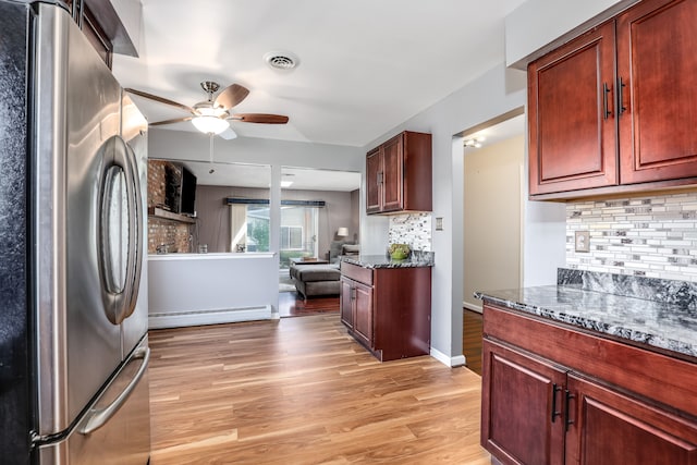 kitchen with dark stone countertops, baseboard heating, tasteful backsplash, light hardwood / wood-style floors, and stainless steel refrigerator