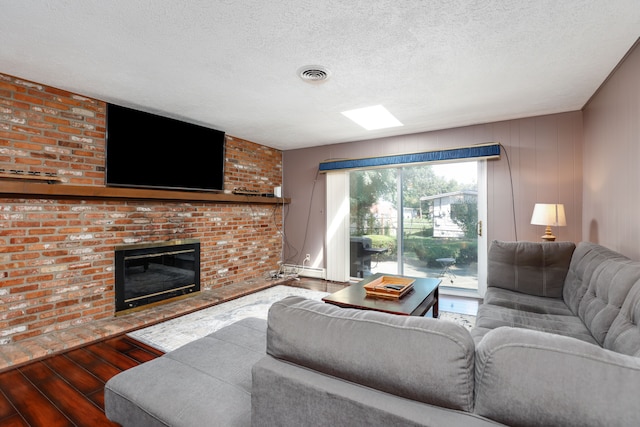 living room featuring a brick fireplace, a textured ceiling, and hardwood / wood-style flooring