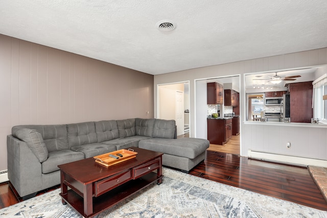 living room featuring ceiling fan, a baseboard heating unit, a textured ceiling, and light hardwood / wood-style flooring