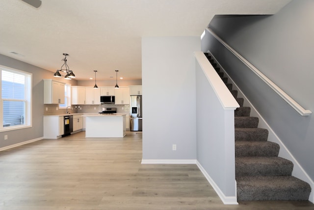 kitchen with a center island, hanging light fixtures, light hardwood / wood-style flooring, white cabinets, and appliances with stainless steel finishes