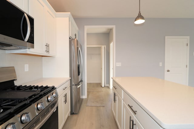 kitchen featuring white cabinetry, hanging light fixtures, stainless steel appliances, tasteful backsplash, and light wood-type flooring