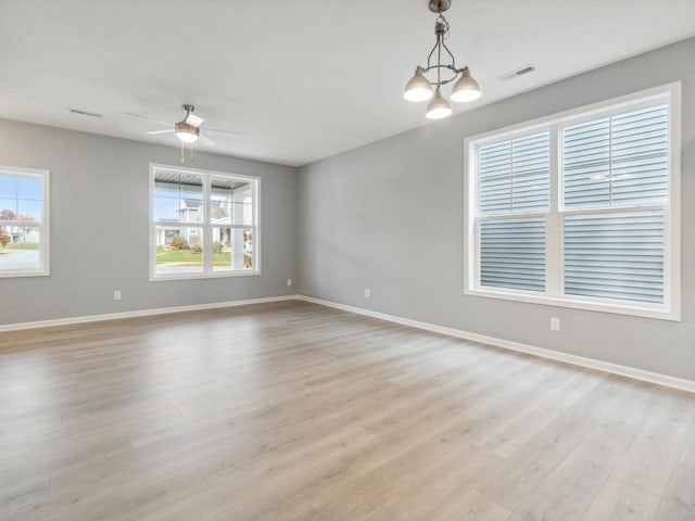 empty room with ceiling fan with notable chandelier and light hardwood / wood-style flooring