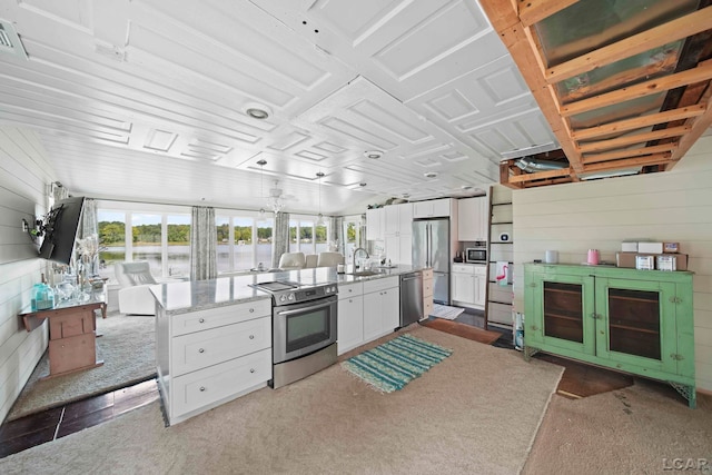 kitchen featuring wood walls, carpet floors, light stone countertops, appliances with stainless steel finishes, and white cabinetry