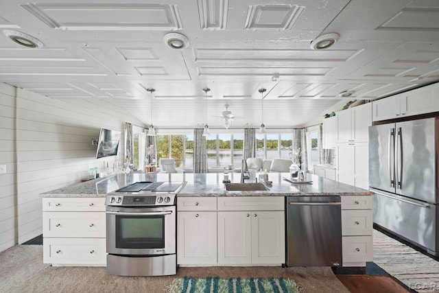 kitchen featuring stainless steel appliances, sink, white cabinets, hanging light fixtures, and wood walls