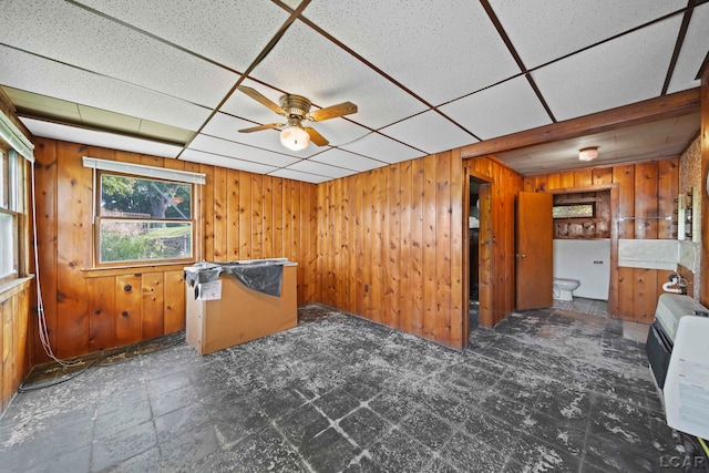 empty room featuring ceiling fan, a drop ceiling, and wooden walls