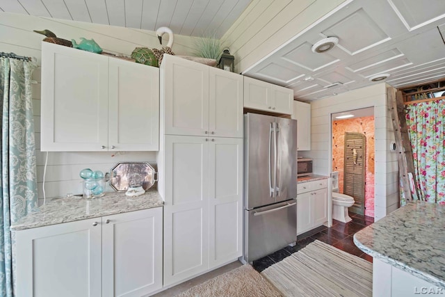 kitchen featuring white cabinetry, light stone counters, wood walls, and appliances with stainless steel finishes