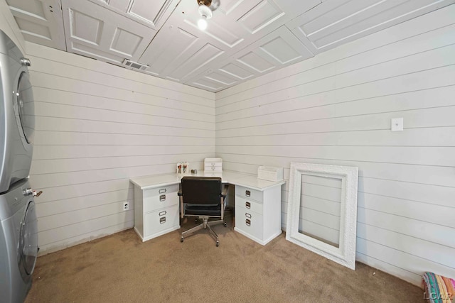 carpeted office space with stacked washer and clothes dryer and wood walls