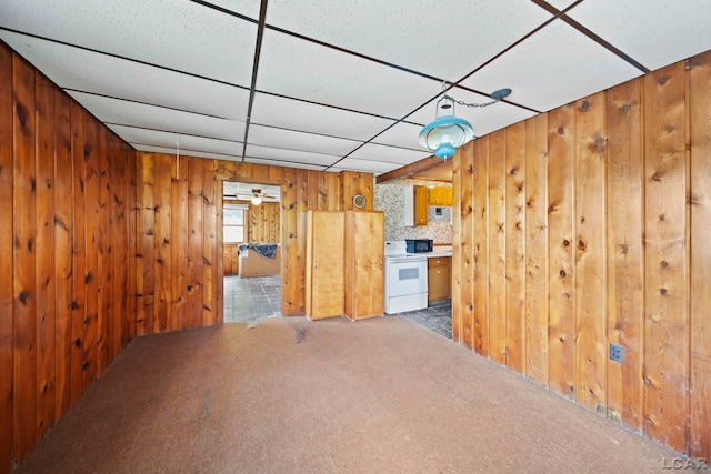 unfurnished living room with carpet flooring, a paneled ceiling, and wooden walls