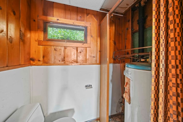 bathroom with water heater, wood walls, and toilet