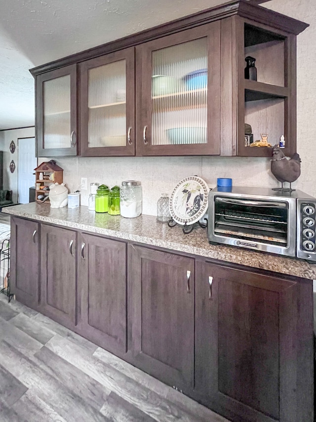 bar featuring backsplash, light wood-type flooring, dark brown cabinetry, and light stone counters