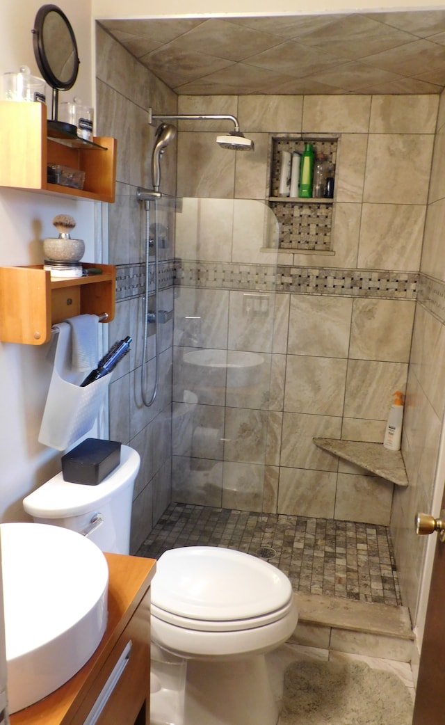 bathroom with tile patterned flooring, a tile shower, vanity, and toilet