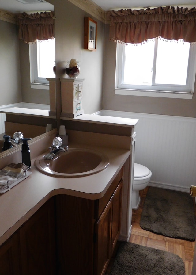 bathroom with parquet flooring, plenty of natural light, vanity, and toilet