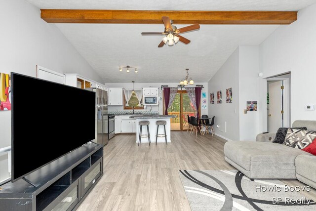 living area featuring light wood-style floors, vaulted ceiling with beams, and ceiling fan with notable chandelier