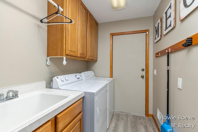 laundry room featuring washing machine and dryer, cabinet space, a sink, and light wood-style flooring
