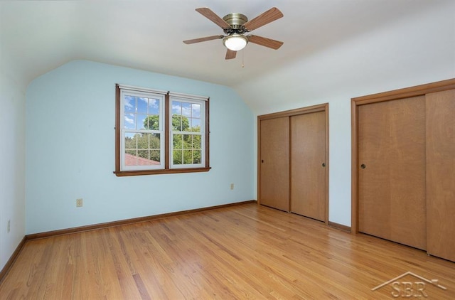 unfurnished bedroom with ceiling fan, two closets, light hardwood / wood-style floors, and vaulted ceiling